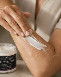 Person applying Wild Alaska Body Butter to their arm with a jar of the product in the background.